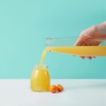 Färskpressad apelsinjuice hälls från en kanna i en glasburk