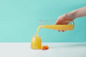 Färskpressad apelsinjuice hälls från en kanna i en glasburk