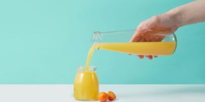 Färskpressad apelsinjuice hälls från en kanna i en glasburk