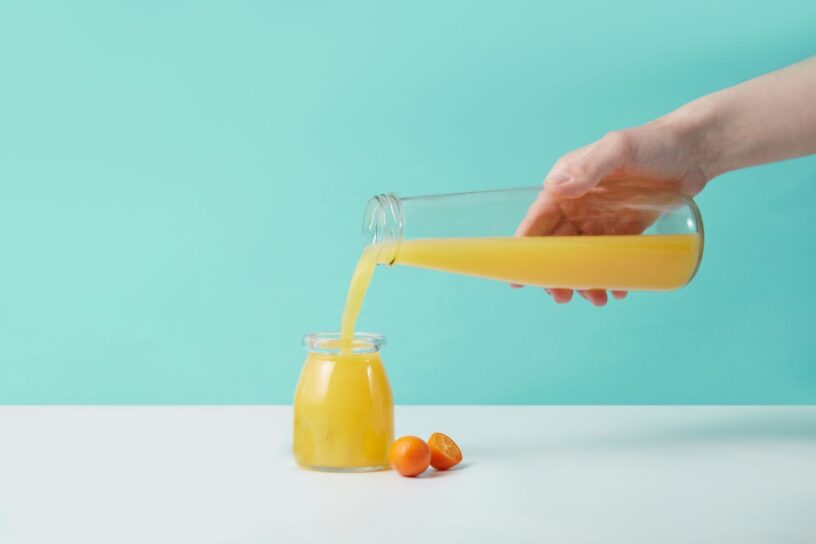 Färskpressad apelsinjuice hälls från en kanna i en glasburk